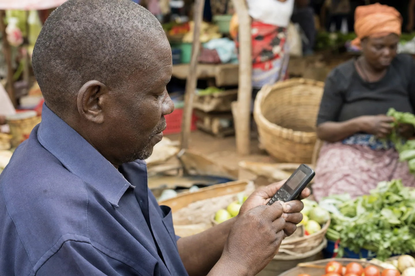 An older Black African man using a feature phone at a market